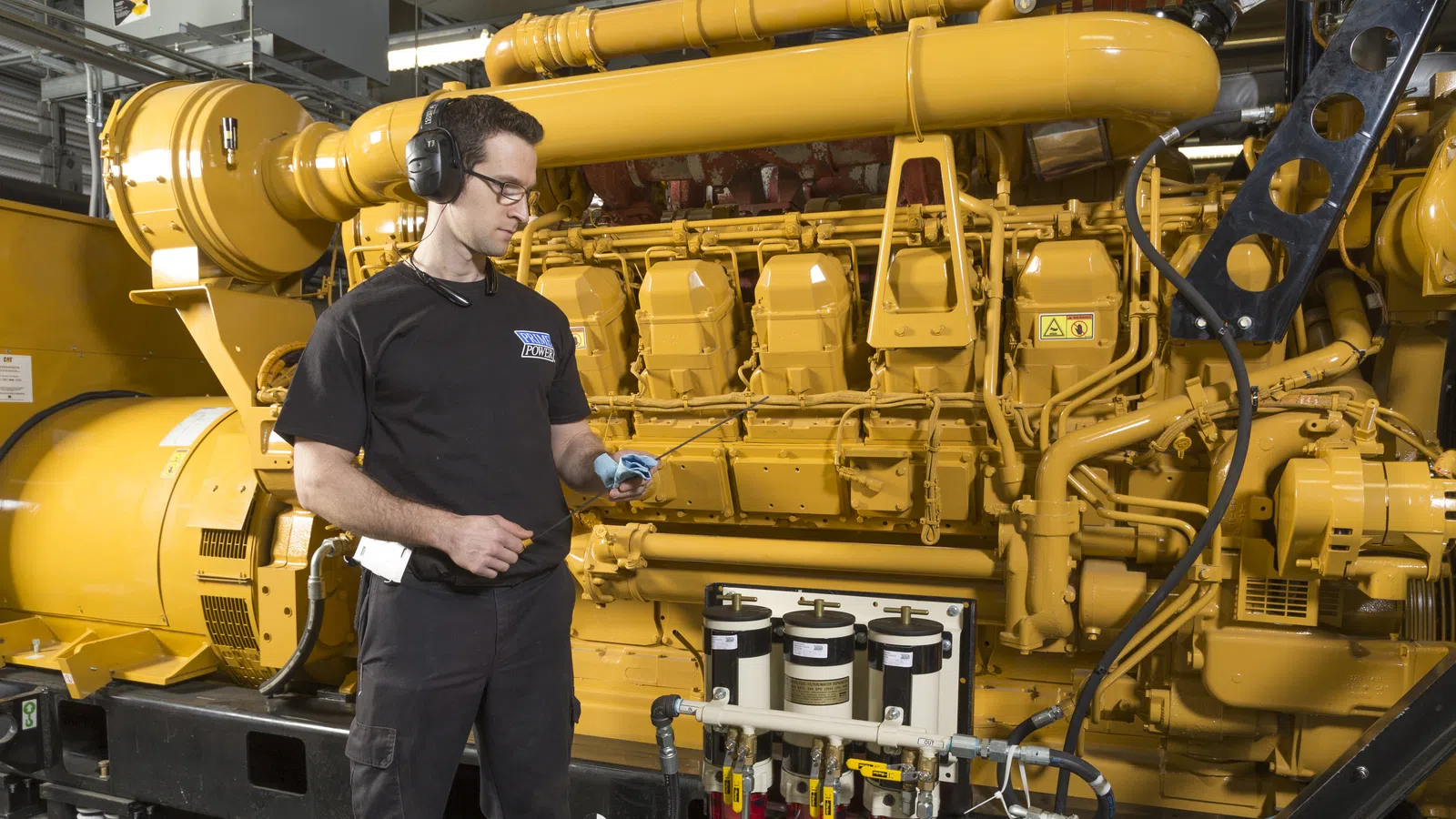 Technician wearing headphones inspecting a large yellow industrial engine with monitoring devices in a factory.