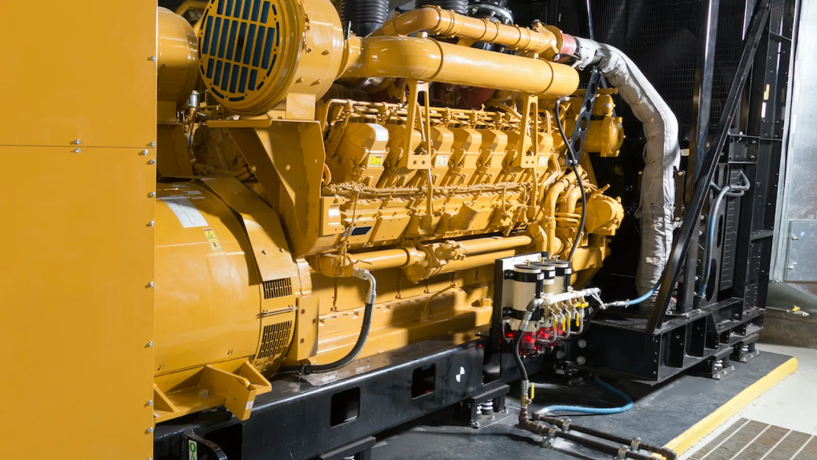 Industrial generator with yellow casing and intricate piping, set in a modern facility.