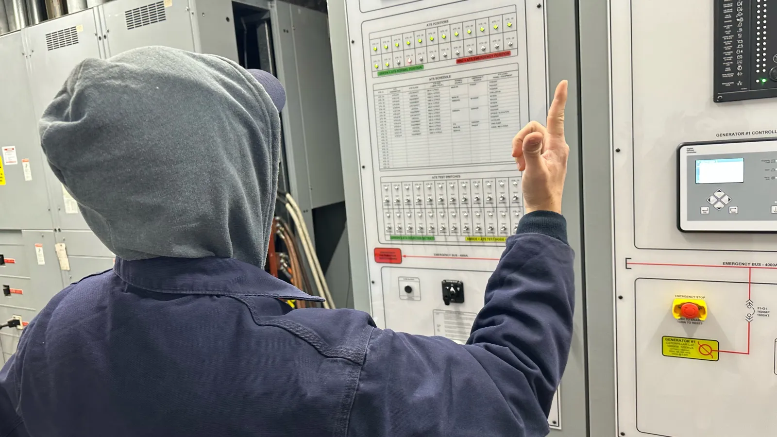 Worker in a hoodie operating control panel with buttons and screens in industrial facility.