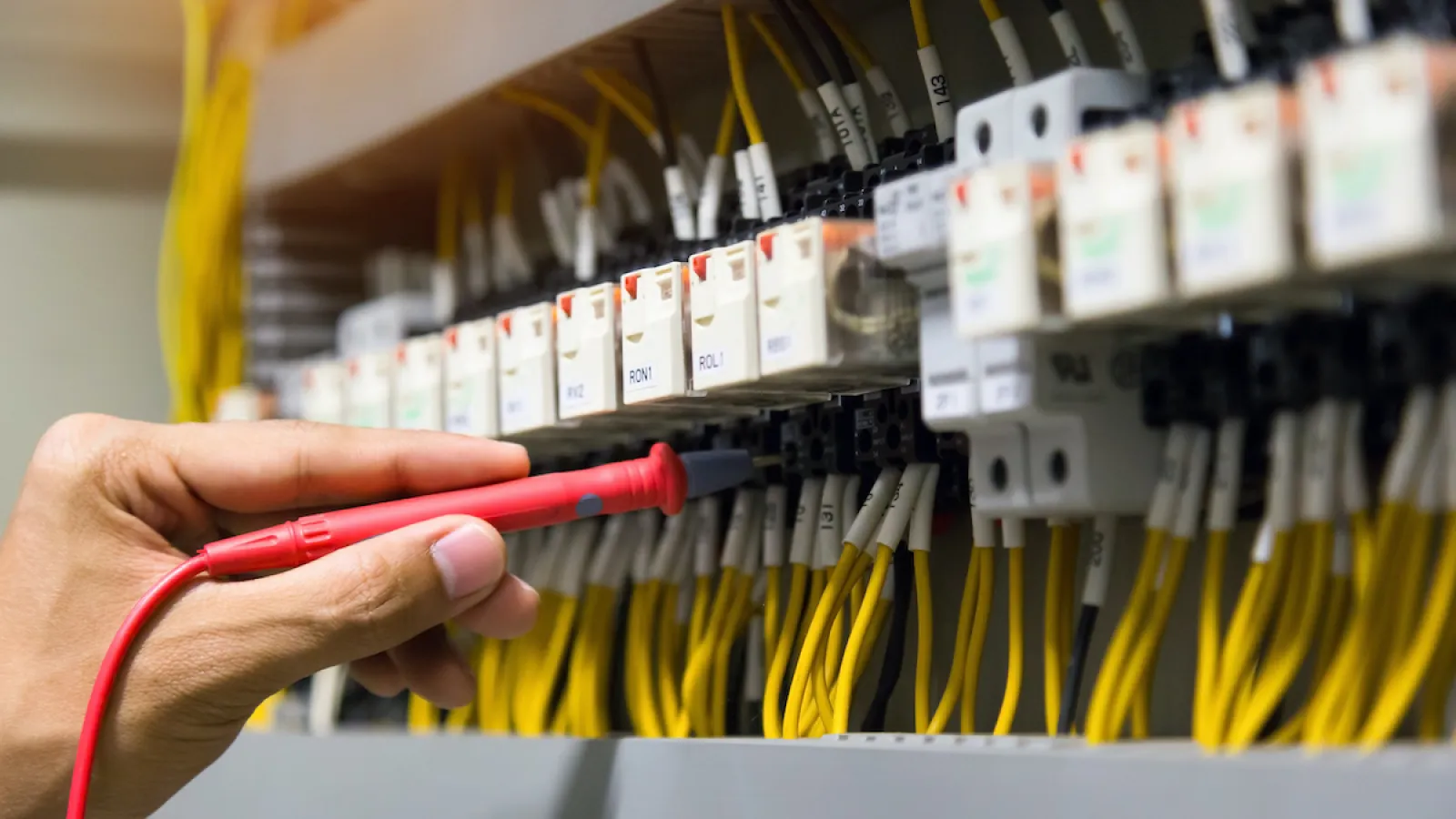 Technician testing electrical connections with a red probe on a circuit breaker panel with yellow wires