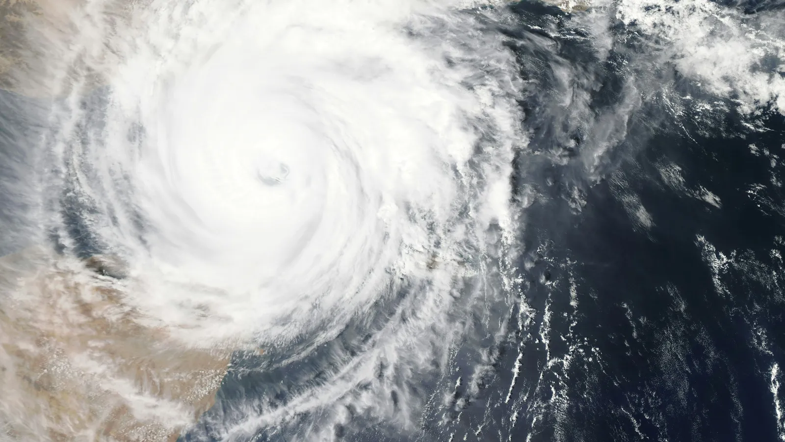 Satellite view of a cyclone with a clear eye over a desert coastal region, swirling clouds over land and sea.