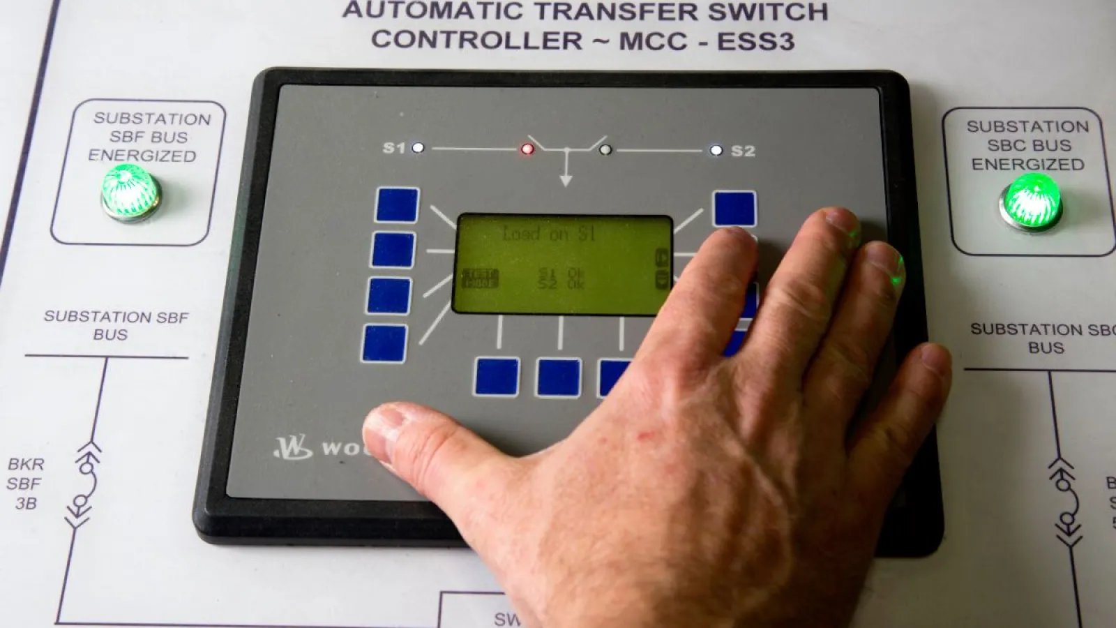 Close-up of an automatic transfer switch controller with a hand pressing buttons and illuminated indicators.