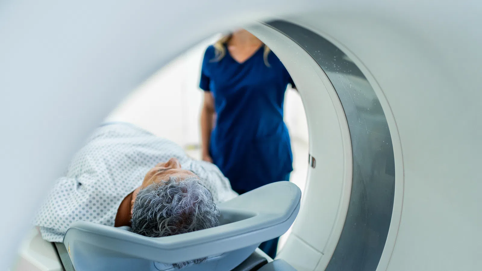 Patient undergoing MRI scan with medical technician in blue scrubs overseeing the procedure in hospital setting