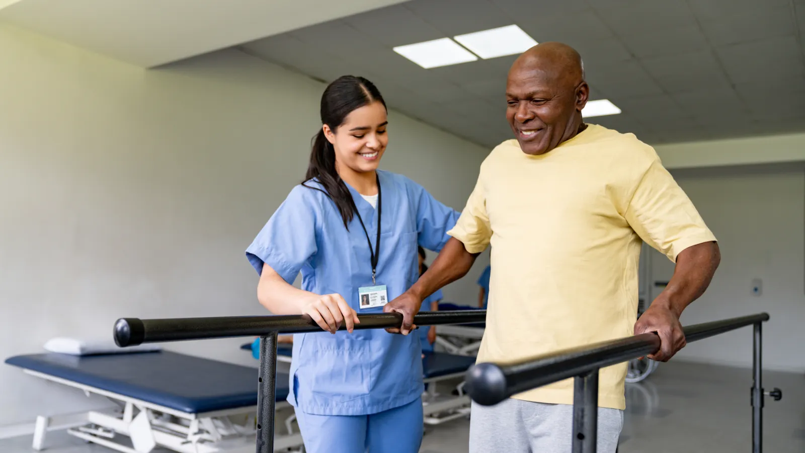 Nurse assisting elderly man with walking bars during physical therapy session in rehabilitation clinic.