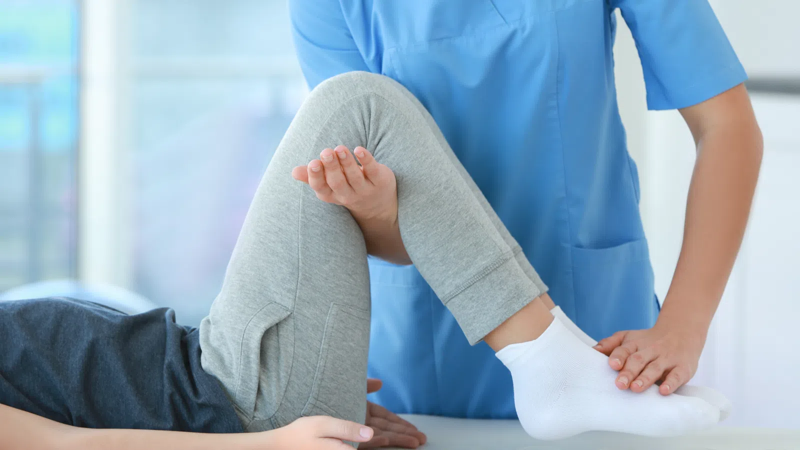 Physical therapist assisting patient with leg stretch during rehabilitation session indoors.