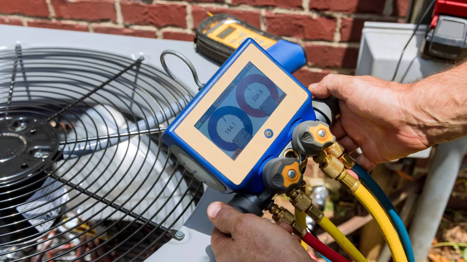 Technician using digital manifold gauge to check pressure on outdoor air conditioning unit with brick wall background