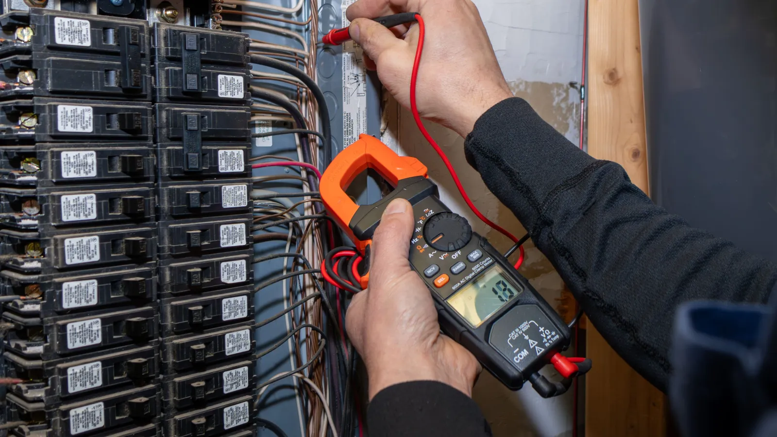 Electrician using a digital multimeter to check wiring in an electrical panel with circuit breakers.