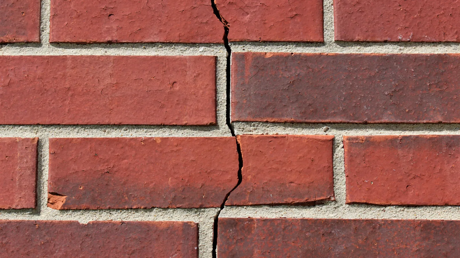 Close-up of a red brick wall with a vertical crack running through the bricks and mortar.