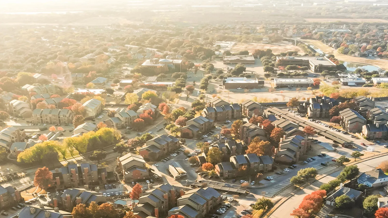 Aerial view of a suburban neighborhood with houses, trees, and roads under bright sunlight.