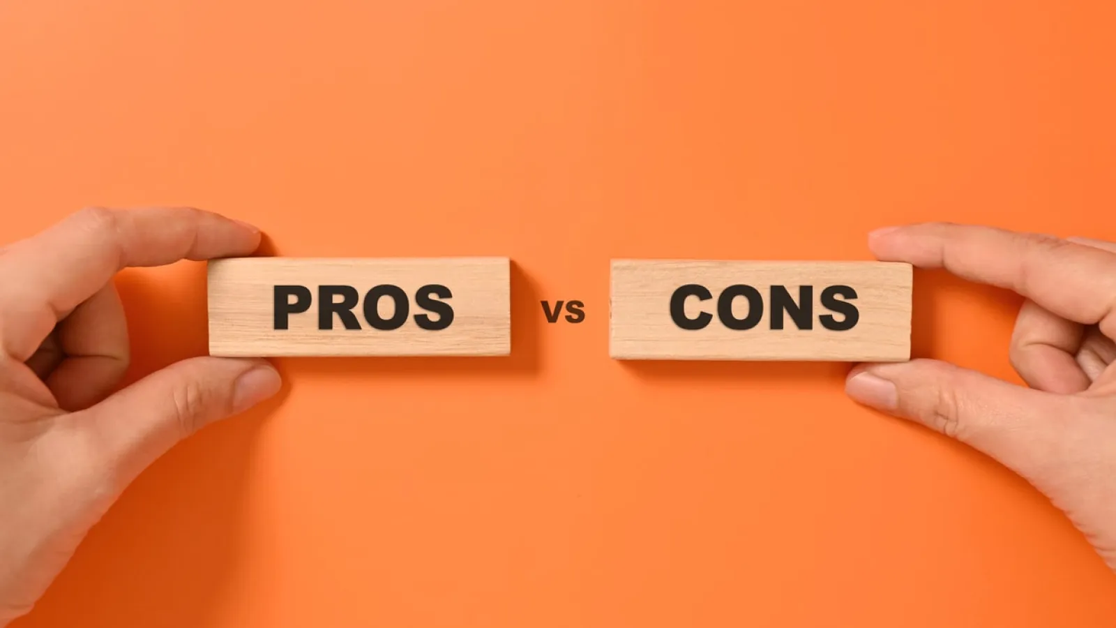 Hands holding wooden blocks labeled PROS and CONS against an orange background with vs text between.