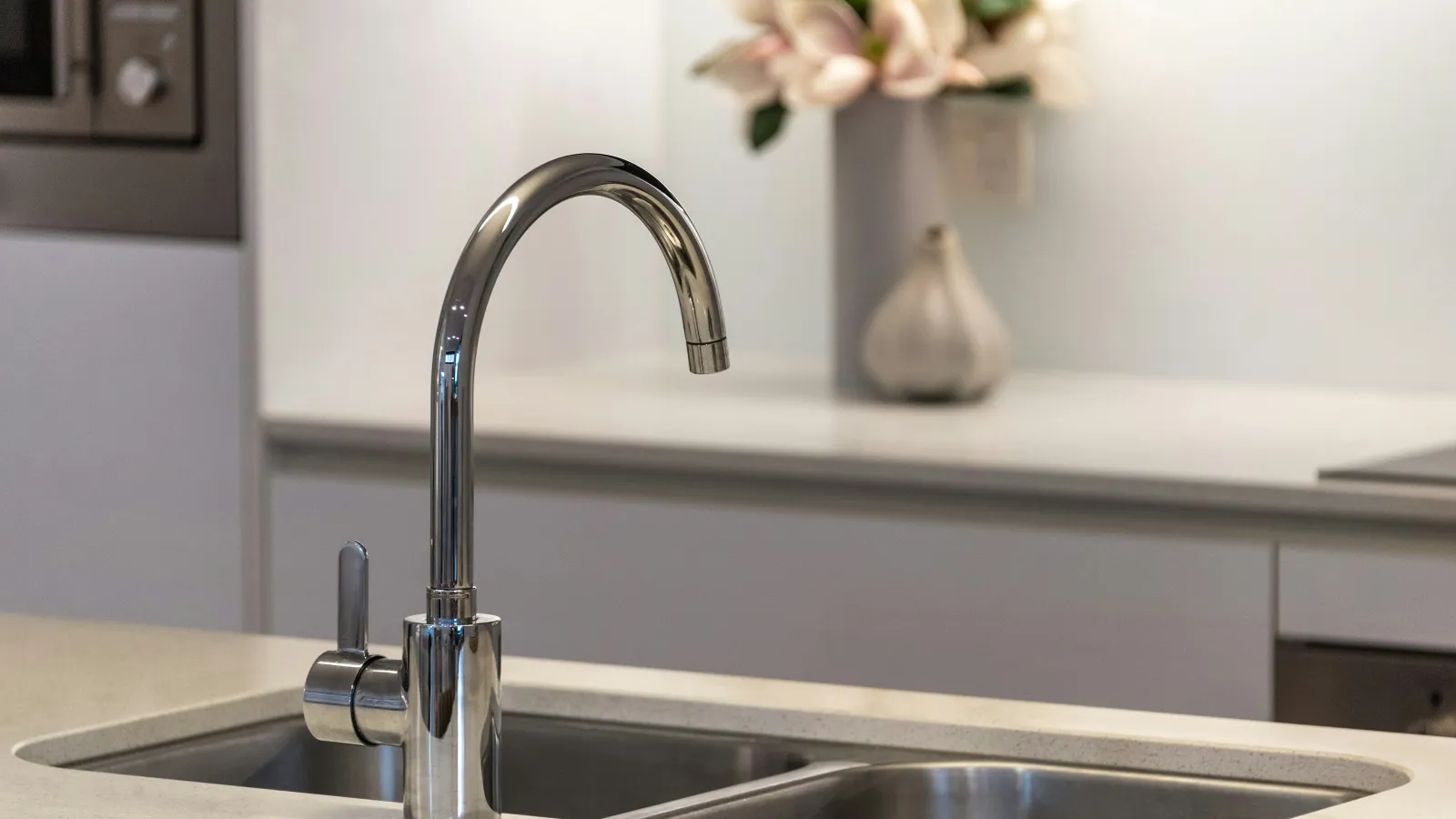 Modern kitchen sink with stainless steel faucet and double basin under clean countertop with blurred flowers in background