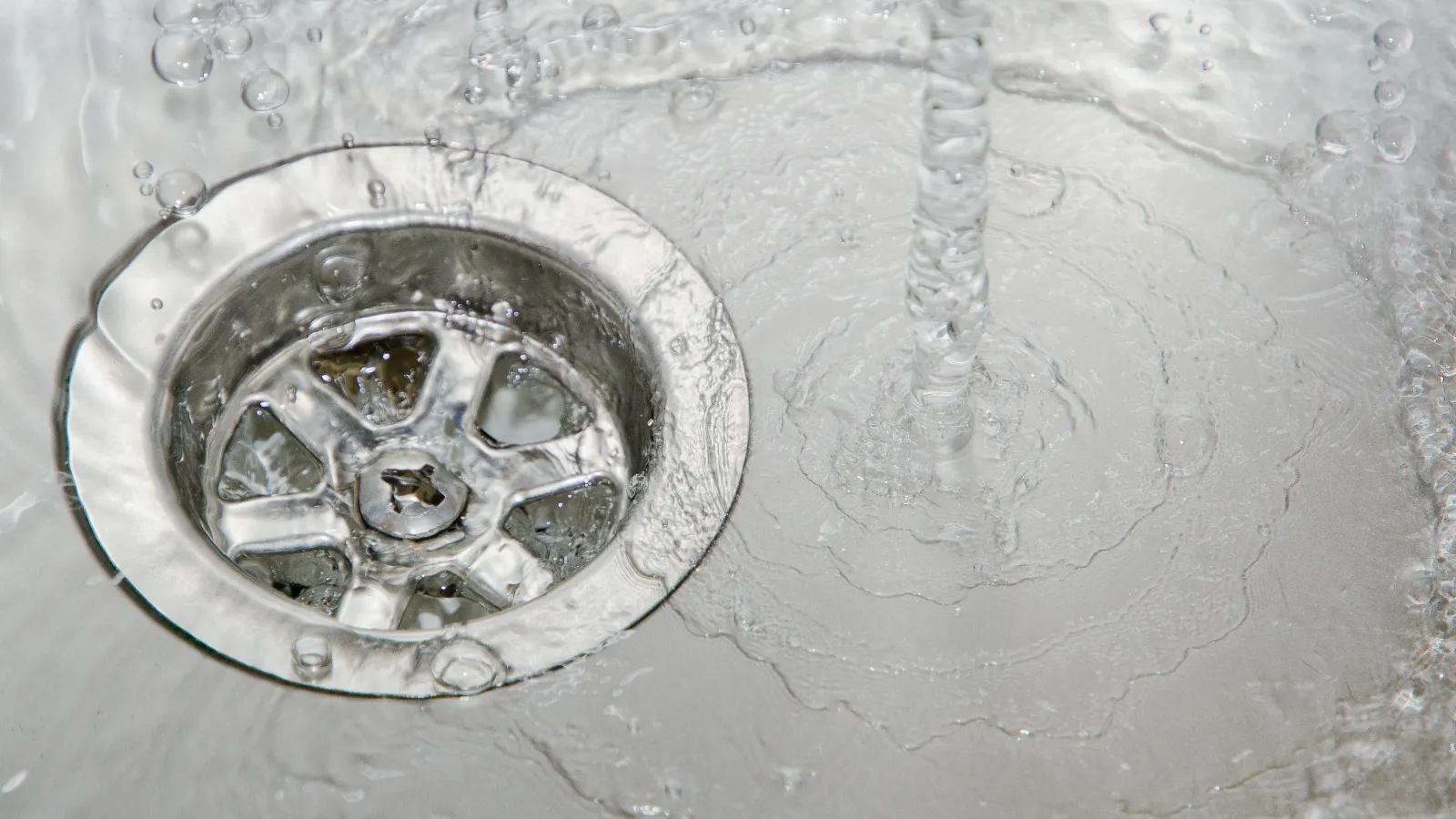 Close-up of water flowing into a metal sink drain with visible ripples and bubbles around it