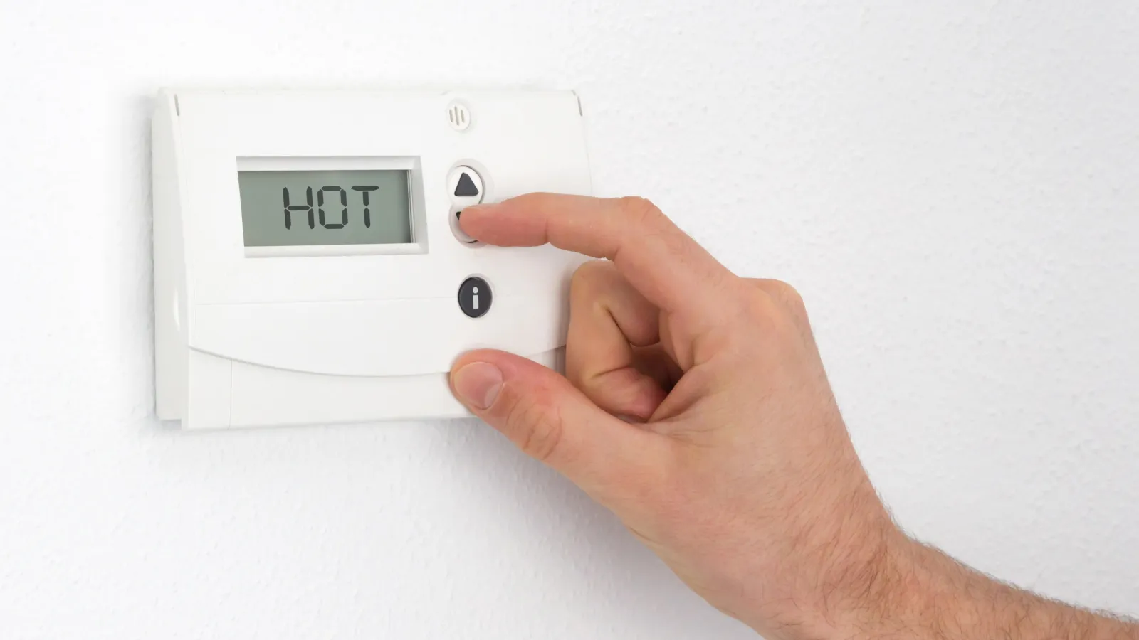 Hand adjusting a white thermostat on a wall displaying the word HOT with temperature control buttons.