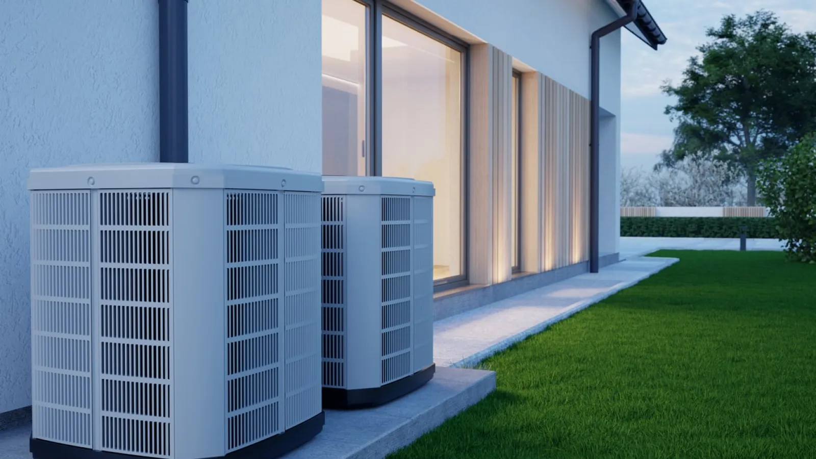 Two modern outdoor air conditioning units installed beside a house with green lawn at dusk