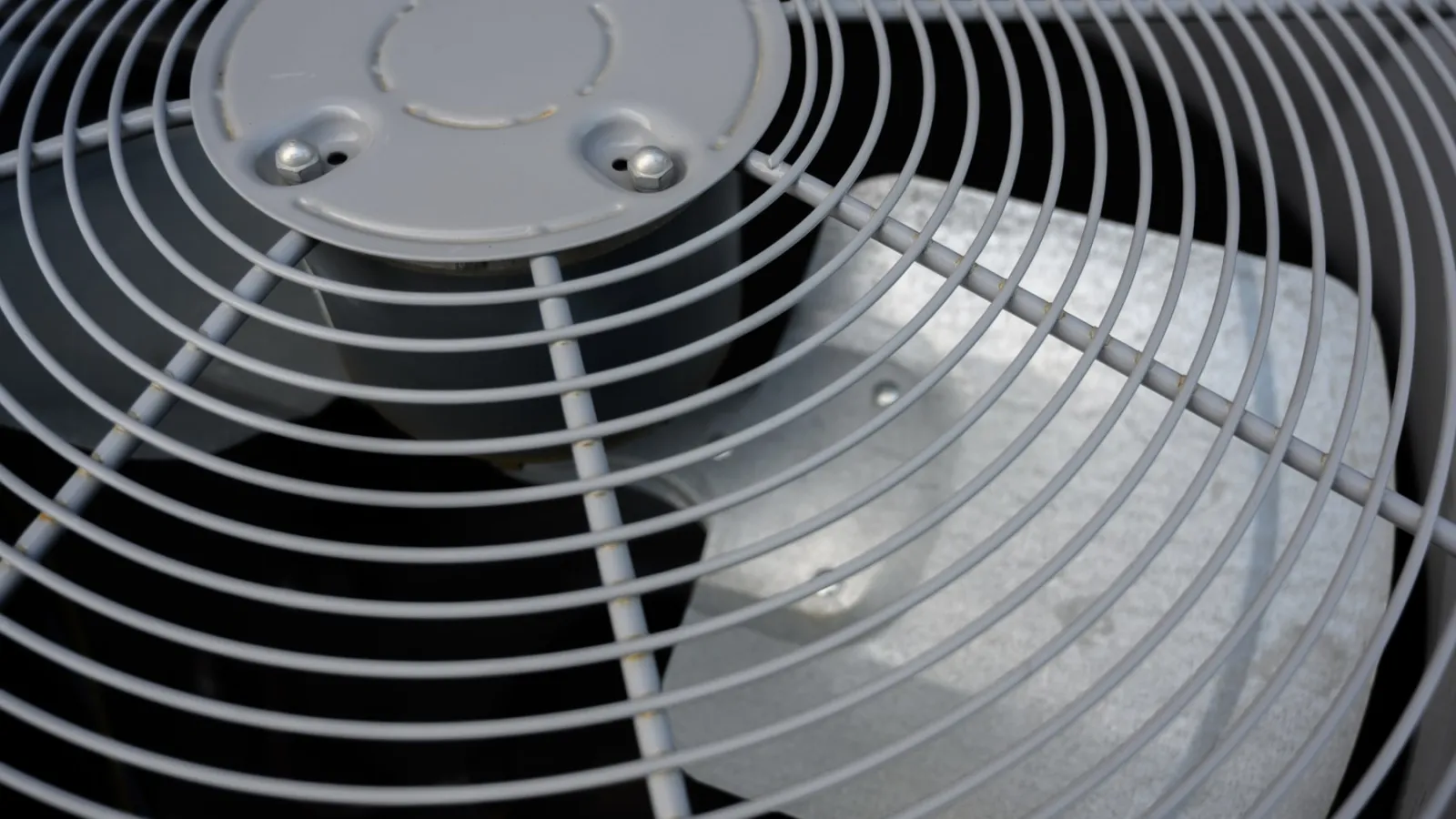 Close-up of a metal fan blade and protective grill on an HVAC outdoor unit.