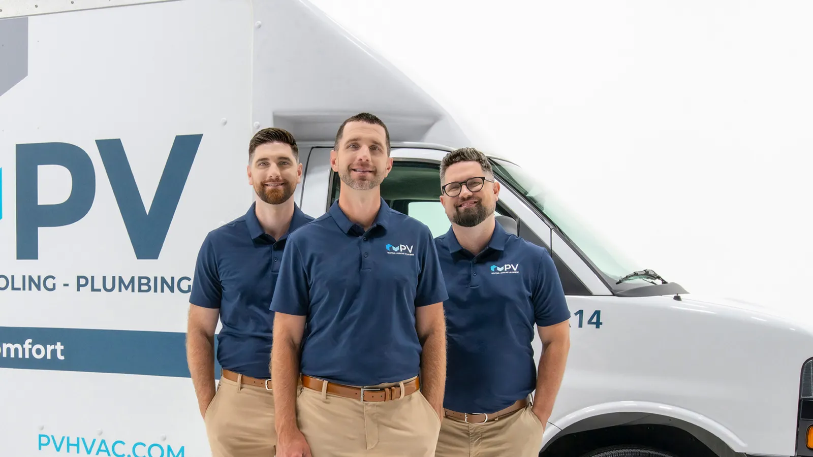 Three men in matching navy polo shirts and khaki pants stand in front of a white service van with PV HVAC branding.