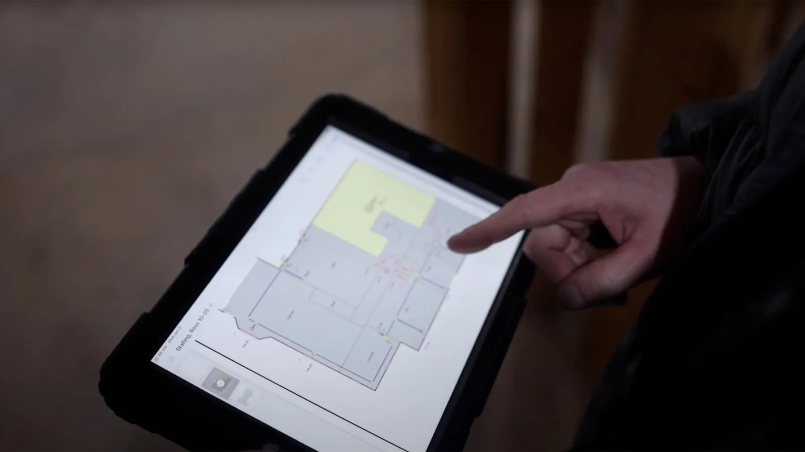 Person using a tablet to view and point at a digital floor plan layout in an indoor setting.