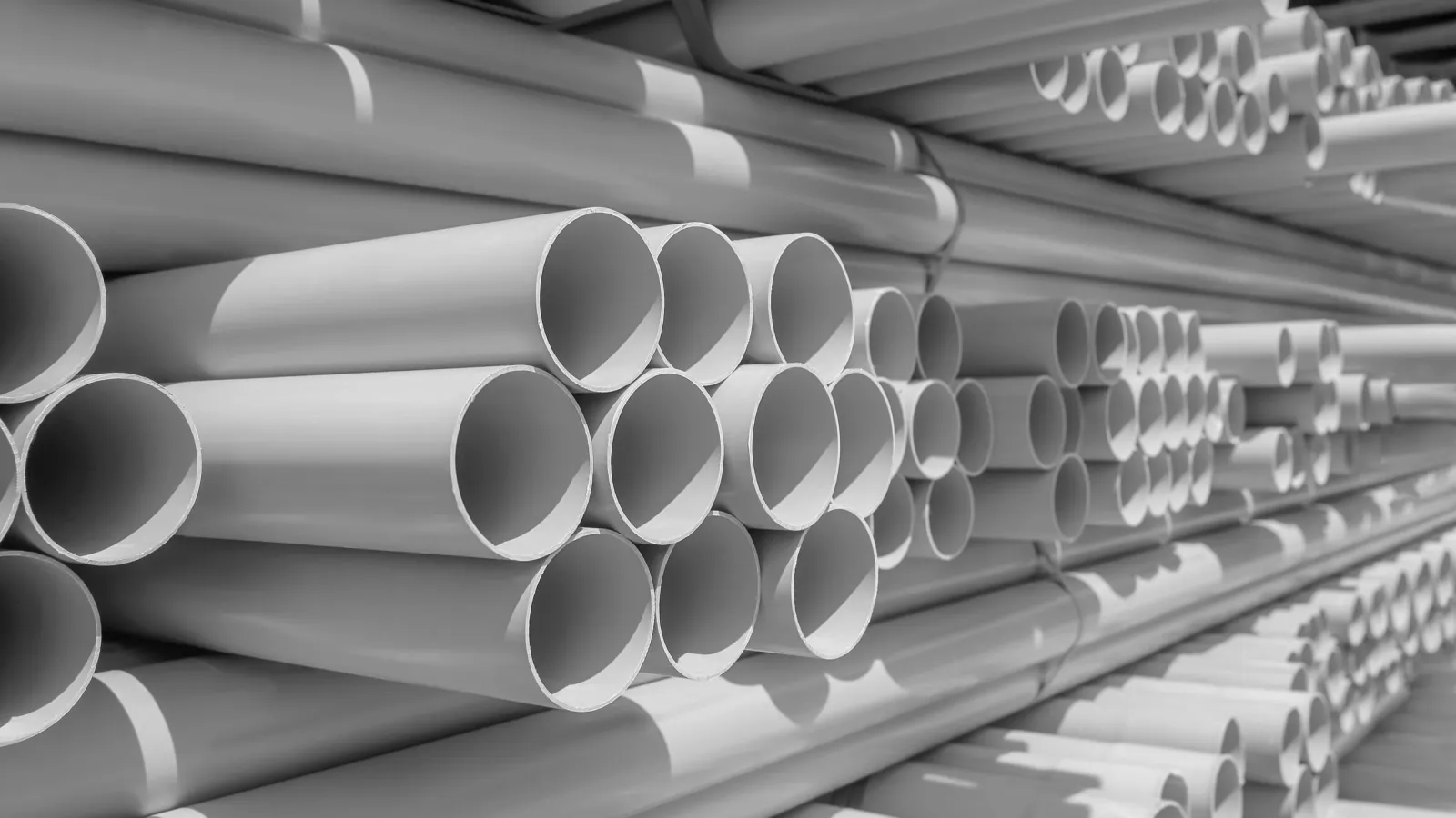 Stack of white plastic PVC pipes arranged in parallel rows for construction or plumbing use.
