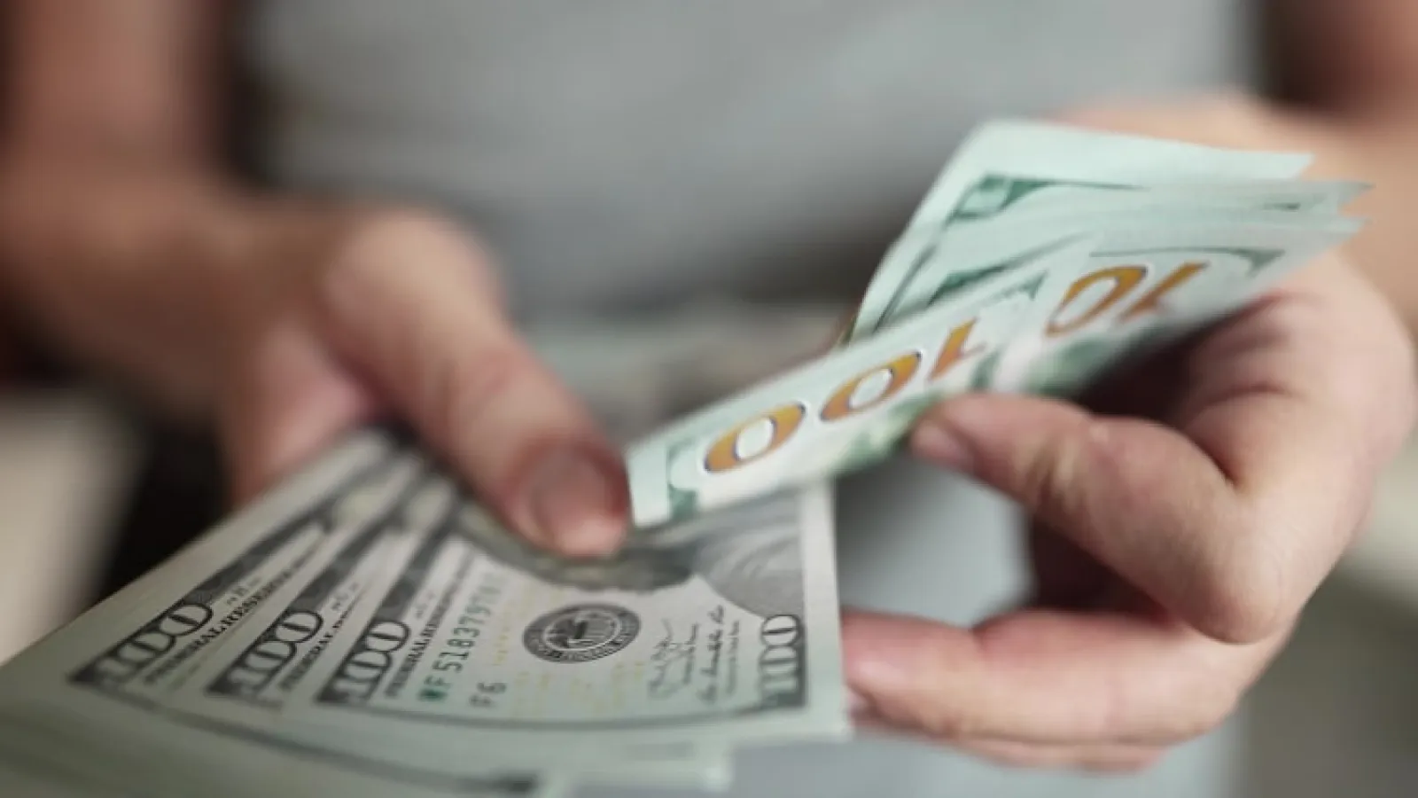 Person counting a stack of US 100 dollar bills with focus on hands and money.