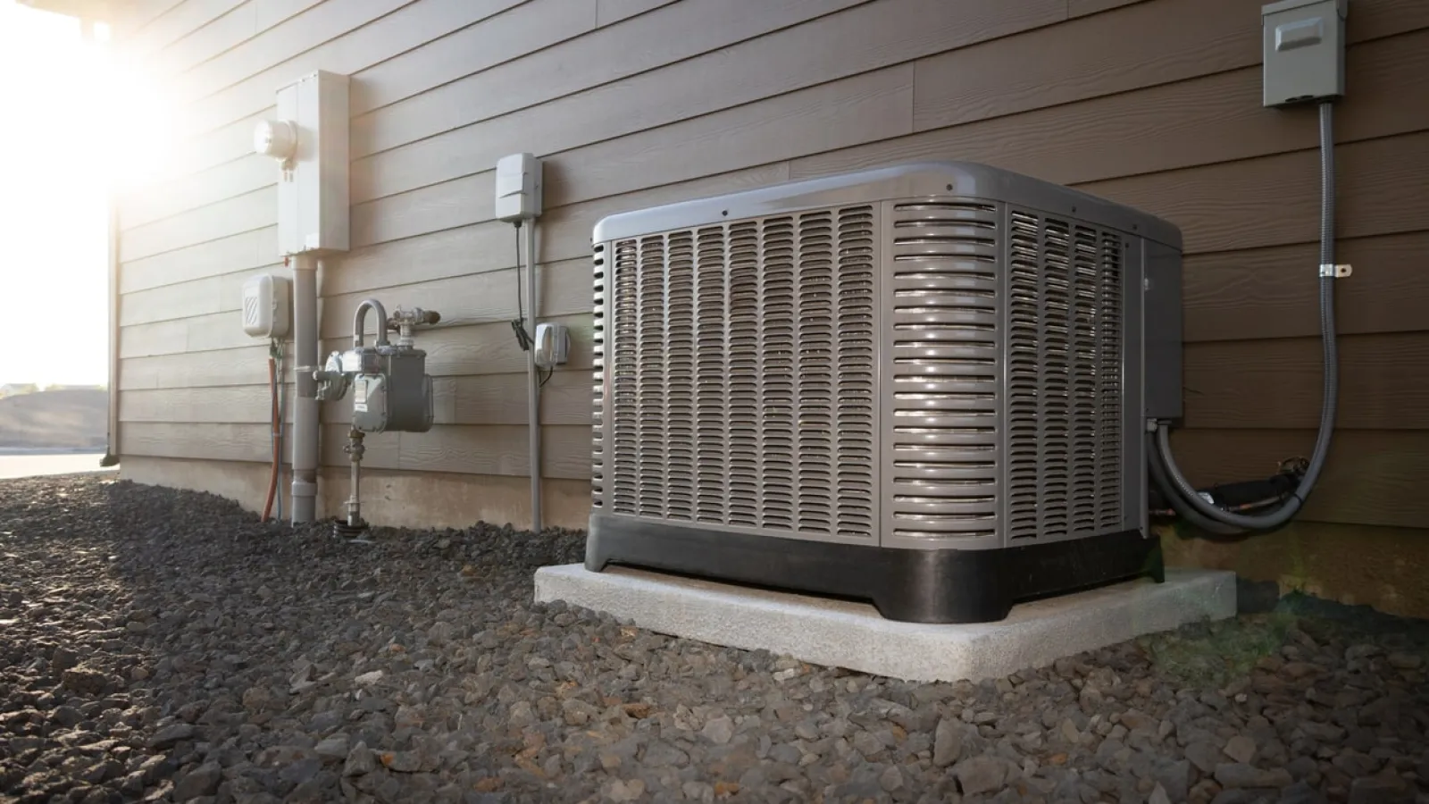 Outdoor air conditioning unit installed on concrete pad beside house with electrical and gas connections.