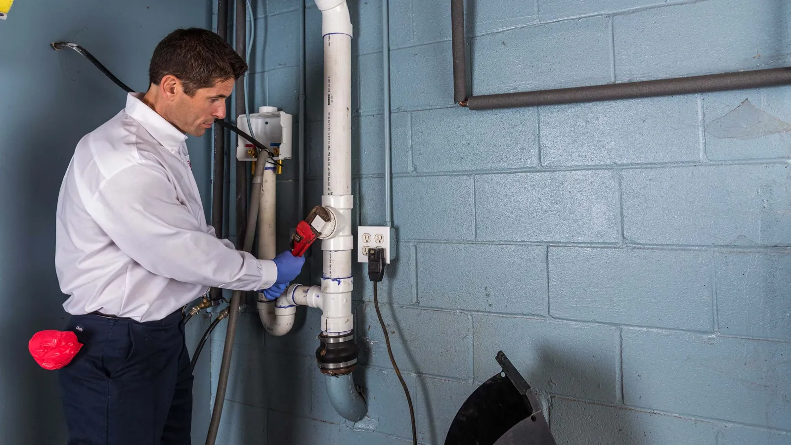 Plumber using a wrench to fix white PVC pipes against a blue wall in a utility room.
