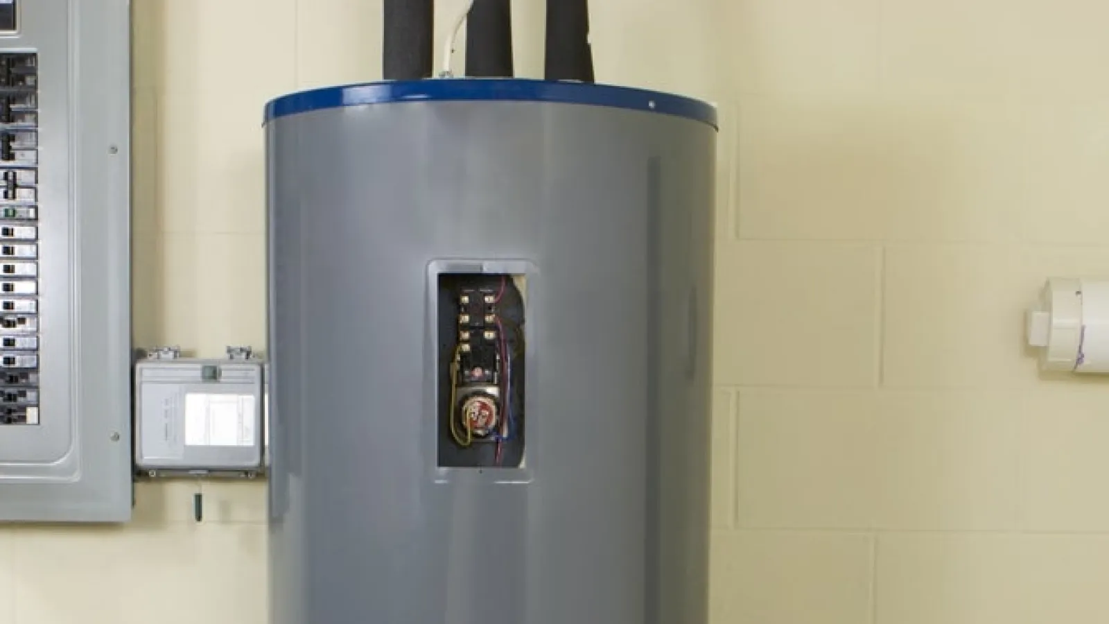 Modern gray water heater installed next to an electrical panel in a clean utility room.