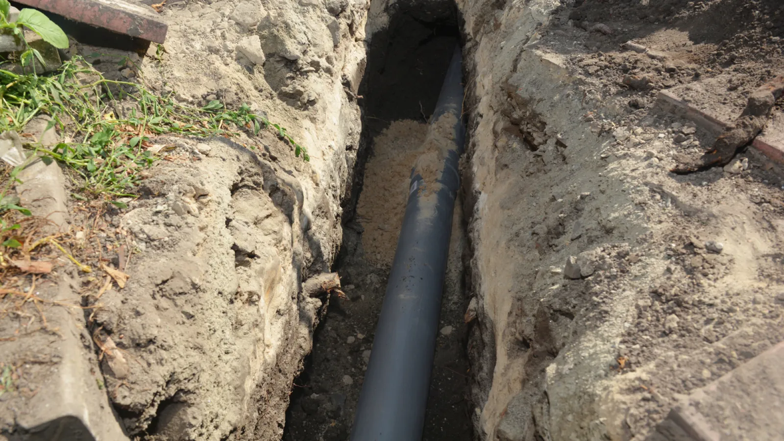 Plastic pipe being installed in a narrow trench dug in soil for underground plumbing or drainage.