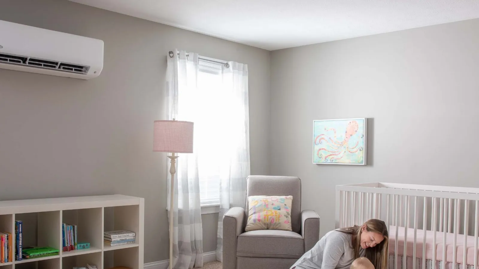 Modern nursery with gray walls, white crib, bookshelf, armchair, and woman organizing baby clothes