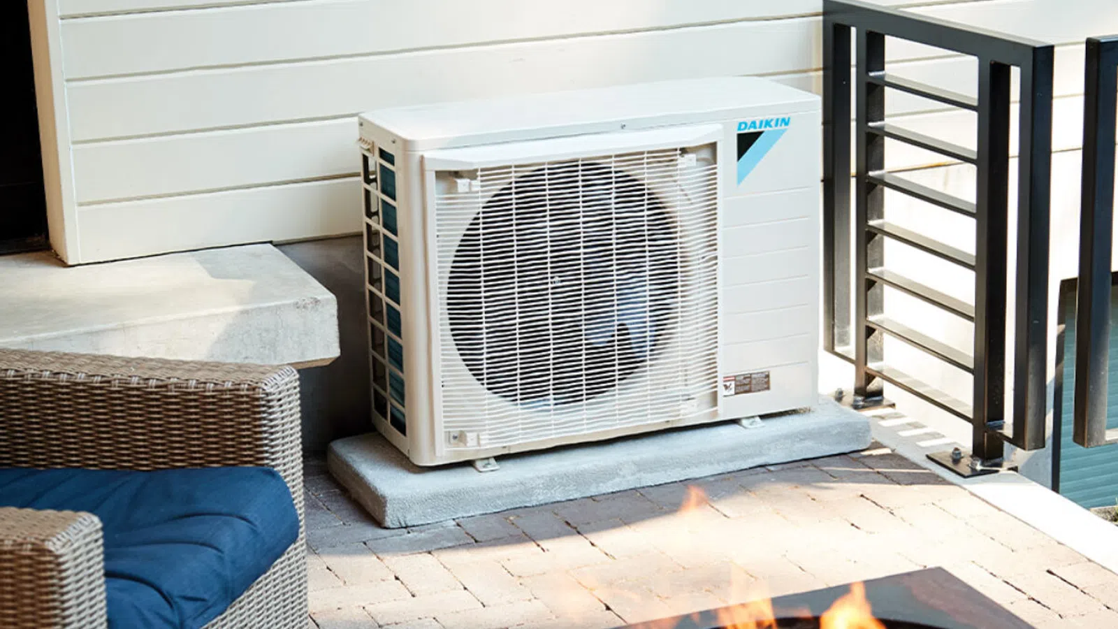 Outdoor Daikin air conditioning unit installed on a patio next to a wicker chair and fire pit.