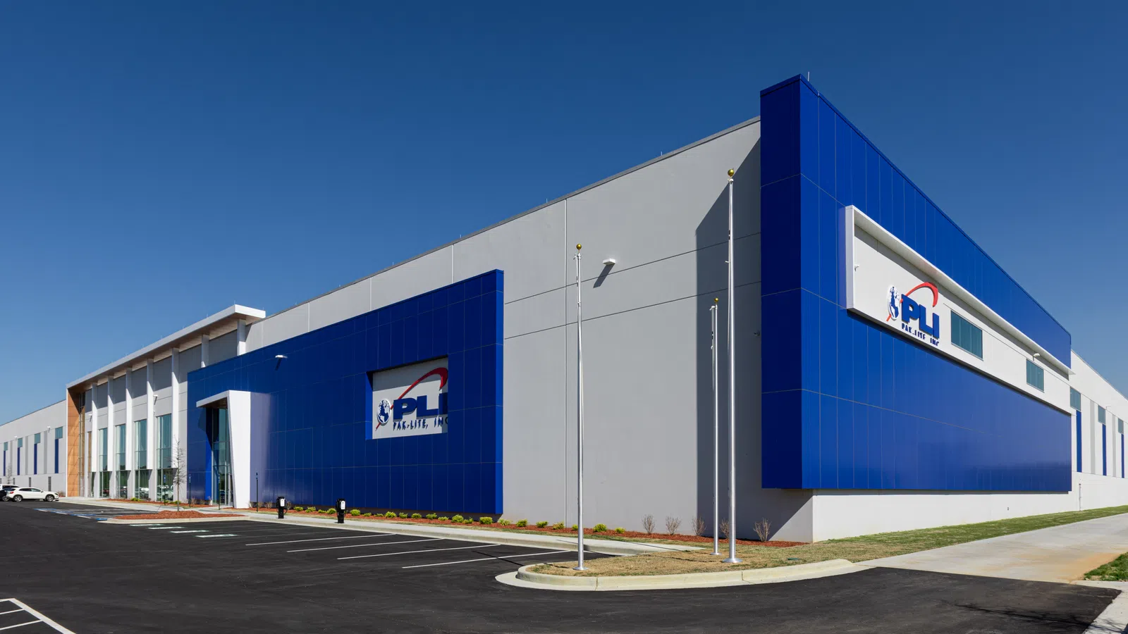 Modern industrial building with blue accents and clear sky, featuring PL company logos on the facade.