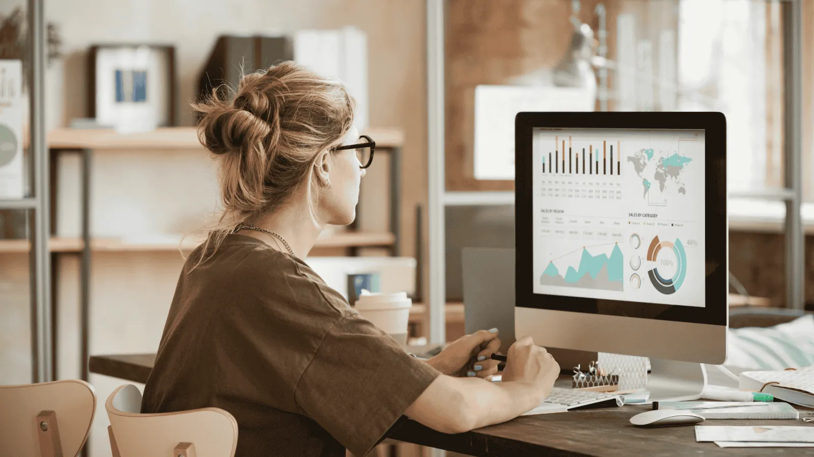 Woman analyzing sales data and charts on a desktop computer in a modern office setting