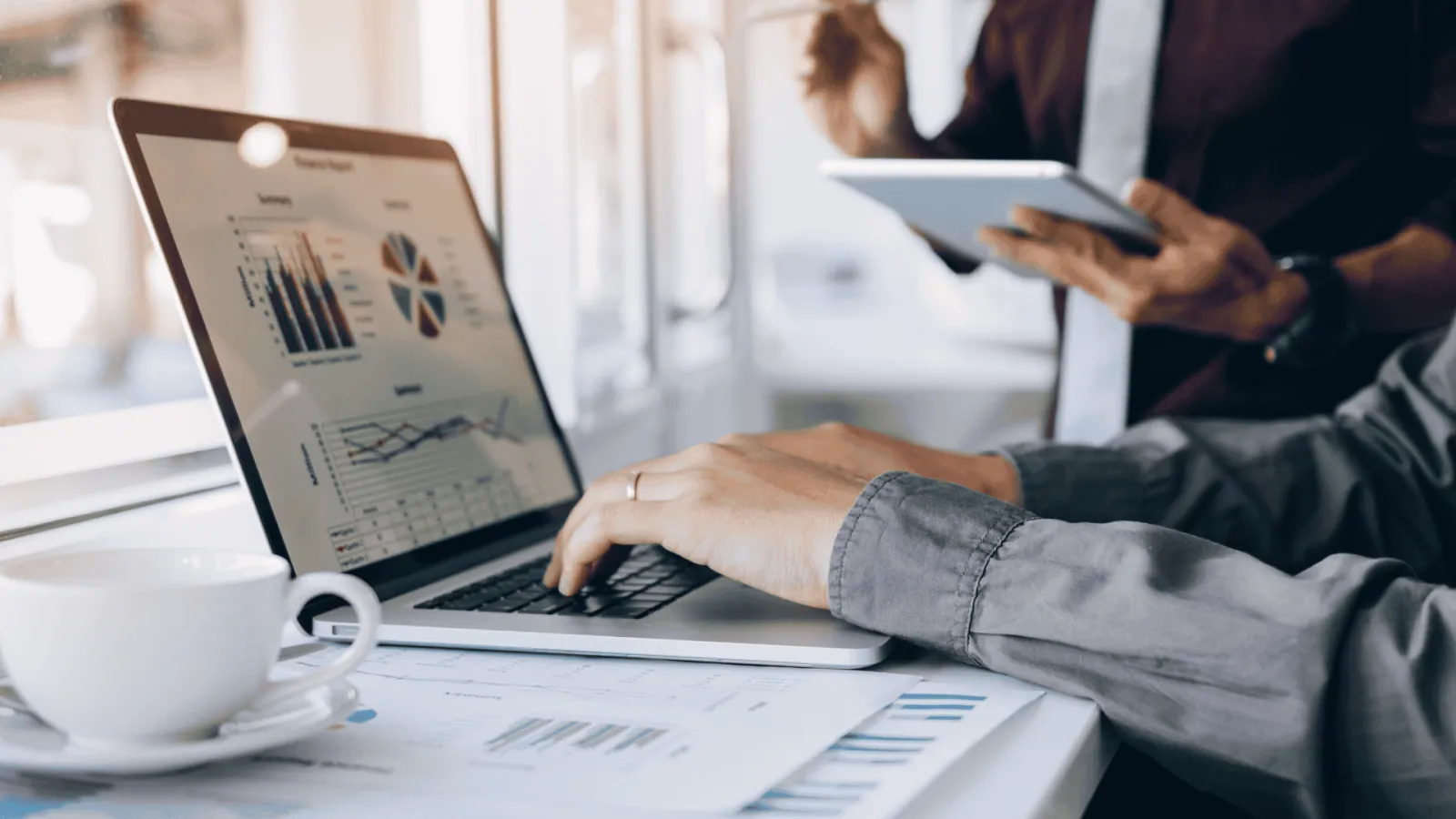 Person analyzing business charts and graphs on laptop and tablet with coffee cup nearby