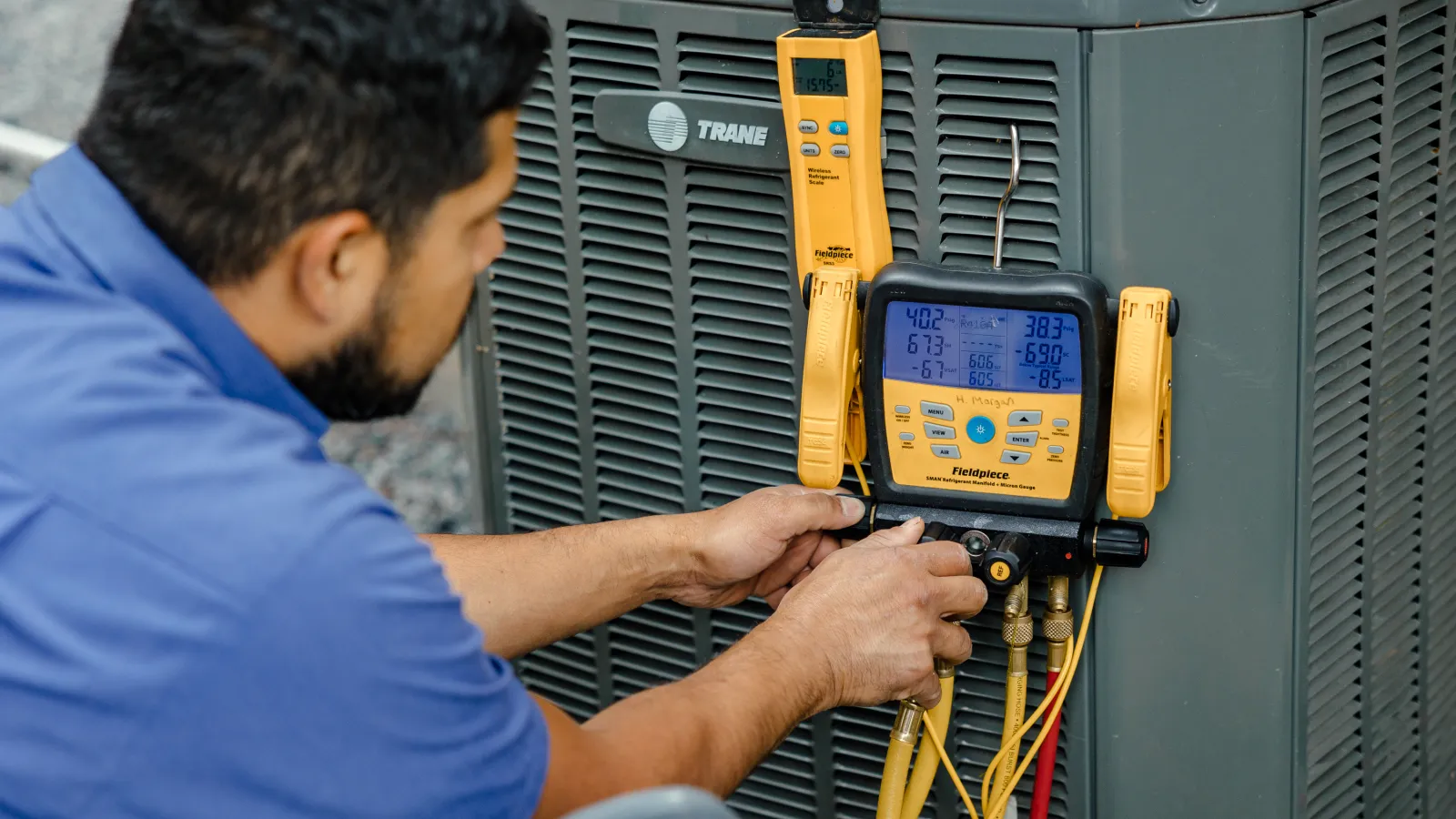 Technician servicing Trane air conditioning unit using yellow digital manifold gauge set outdoors