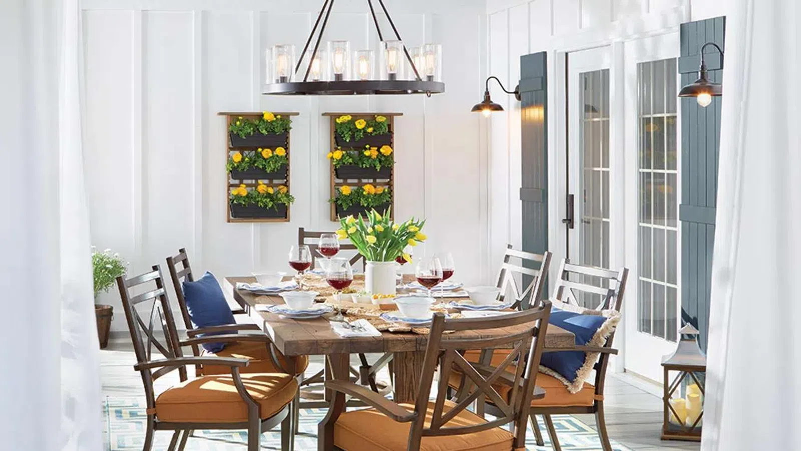 Bright dining room with wooden table, cushioned chairs, floral centerpiece, lemon wall decor, and hanging chandelier.
