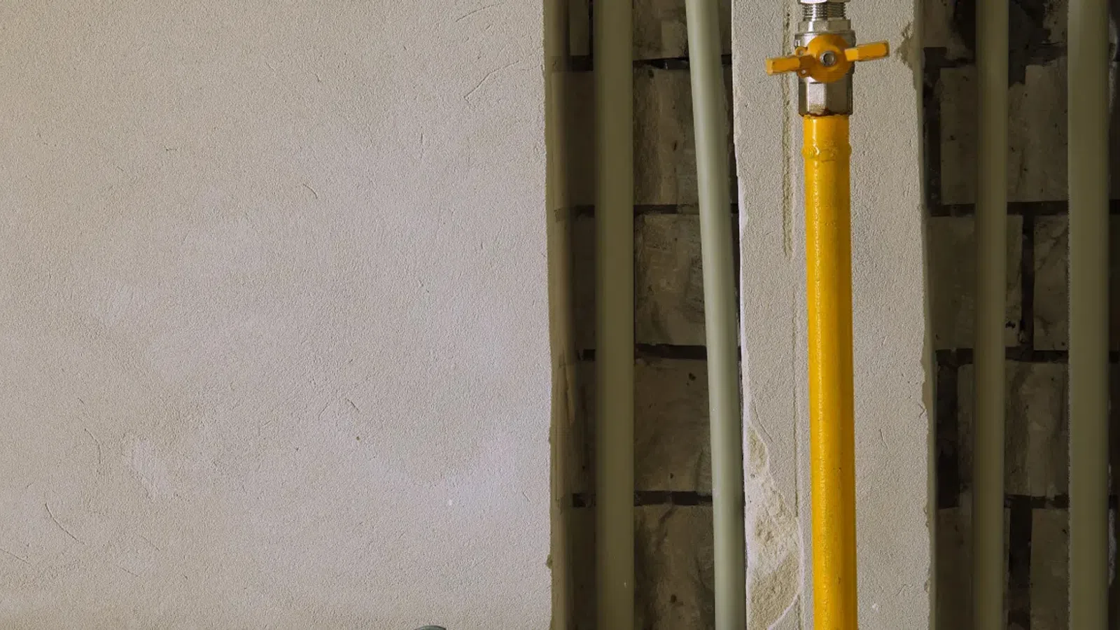Yellow gas pipe with valve installed on a white wall with exposed brick and utility pipes.