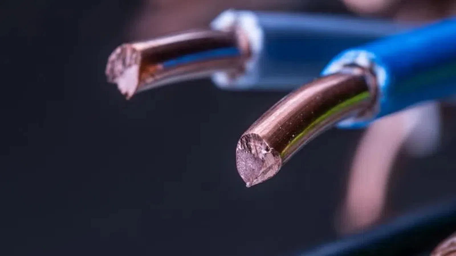 Close-up of exposed copper wires with blue, green, and brown insulation against a dark background.