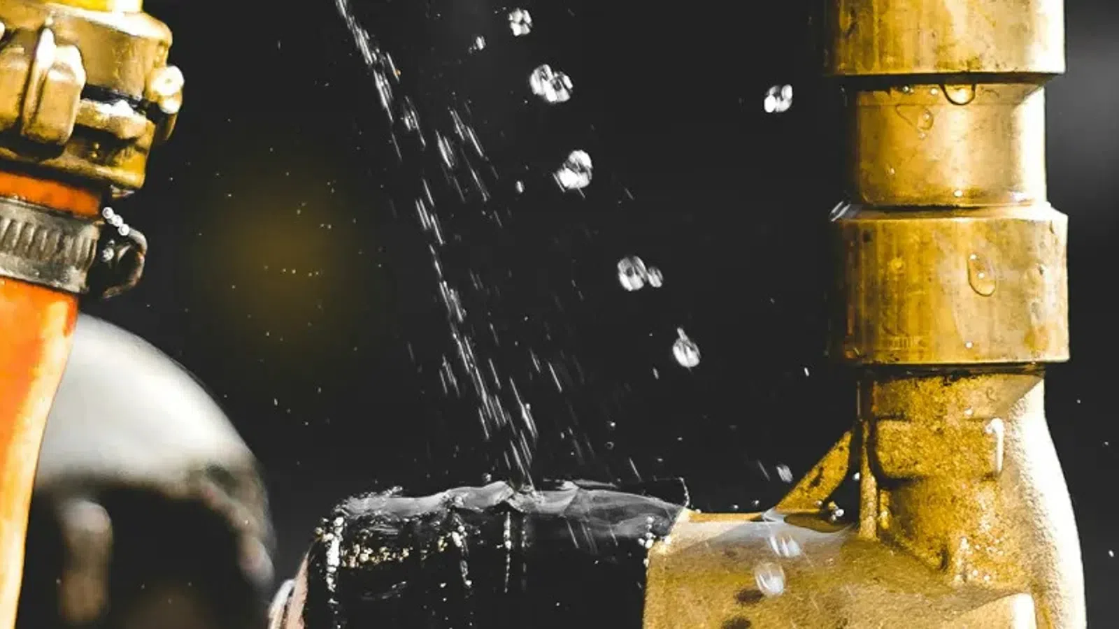 Close-up of a brass valve with leaking water droplets against a dark background and orange hose.