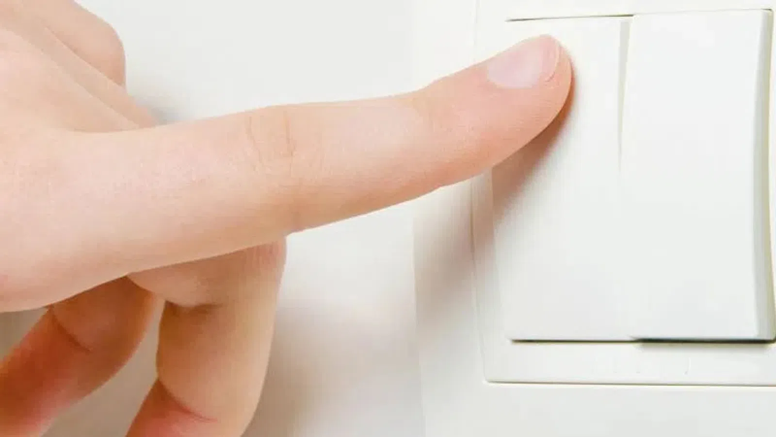 Close-up of a hand turning on a white wall light switch in a bright room.