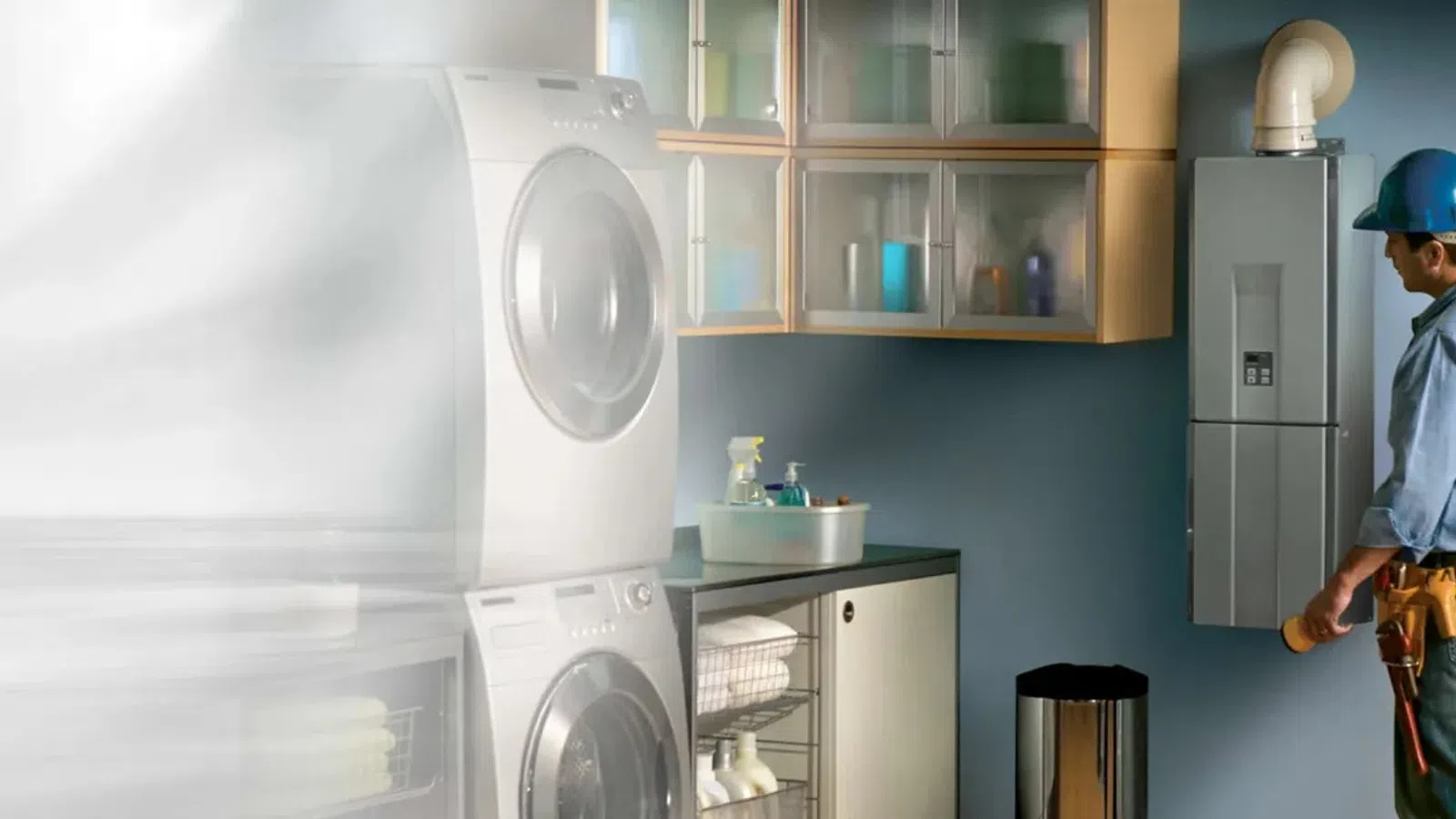 Technician in blue helmet inspects modern furnace in a clean, organized laundry room with washer and dryer.