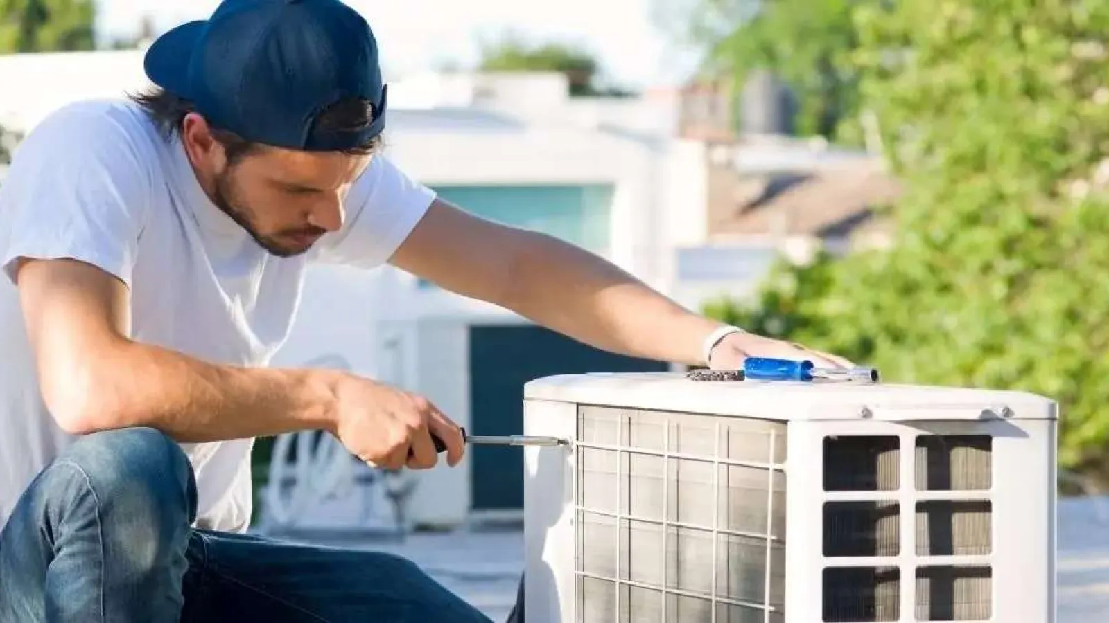 Technician in a blue cap fixing an outdoor air conditioning unit on a rooftop under daylight.