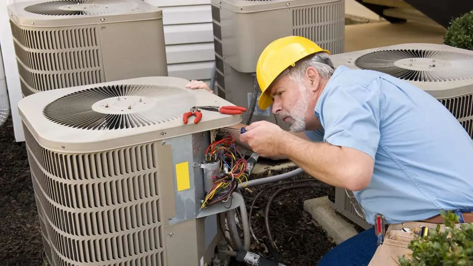 Technician with glasses inspecting and repairing an outdoor HVAC unit during daytime.
