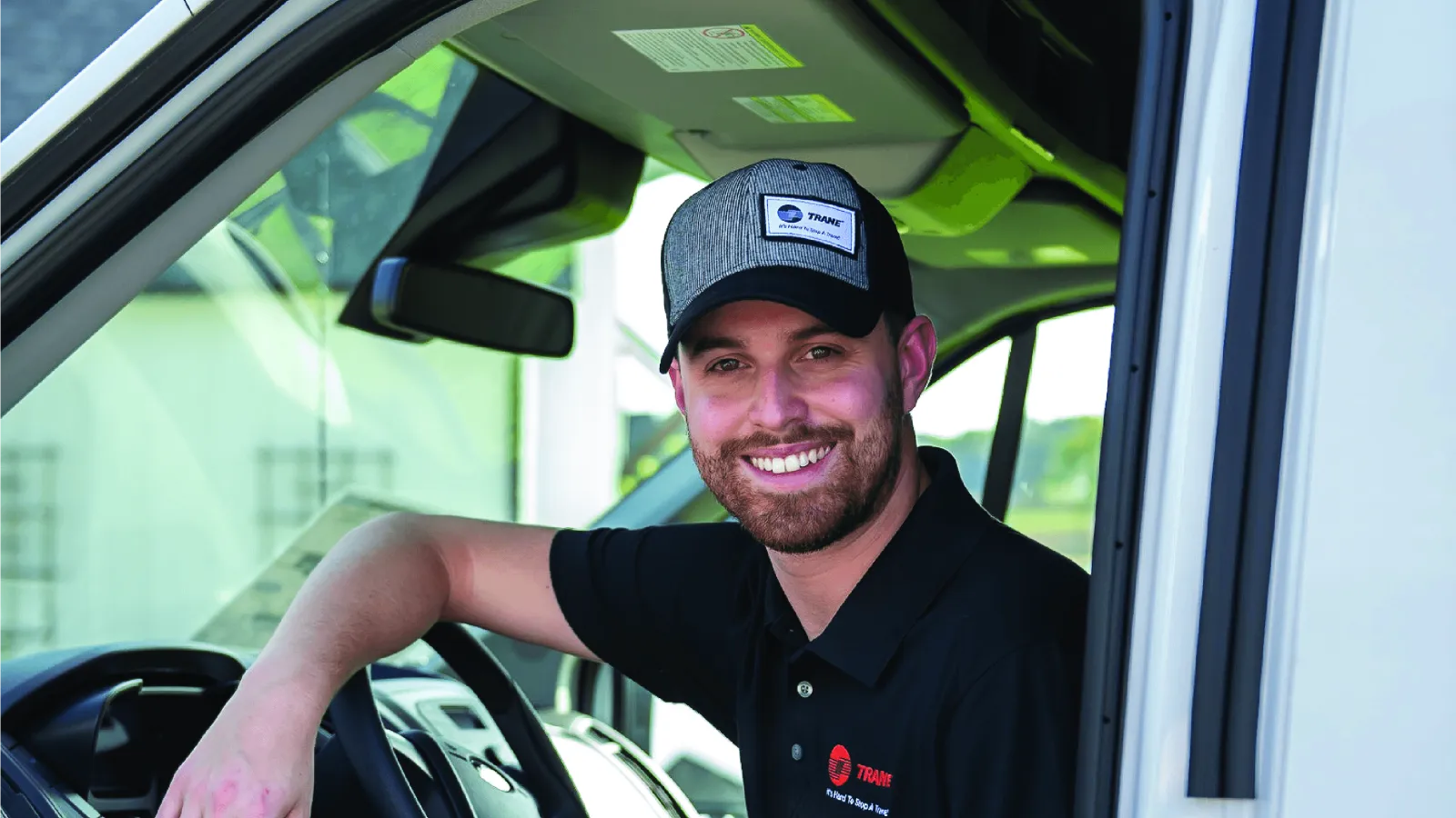 Smiling man wearing a cap and uniform sitting in a white van holding a clipboard, ready for work.