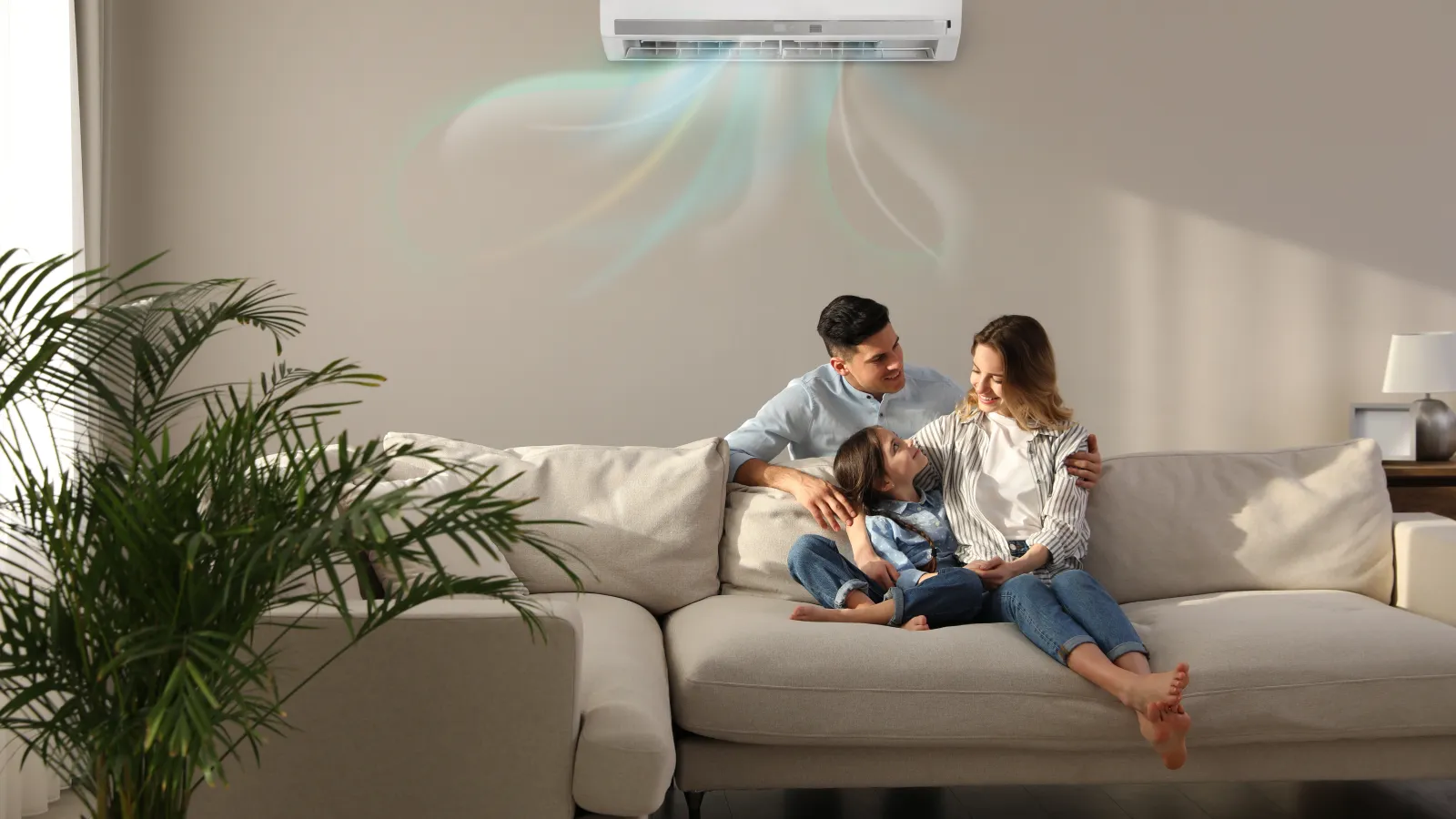 Family of three relaxing on a beige sofa under a wall-mounted air conditioner with cool airflow visualized.