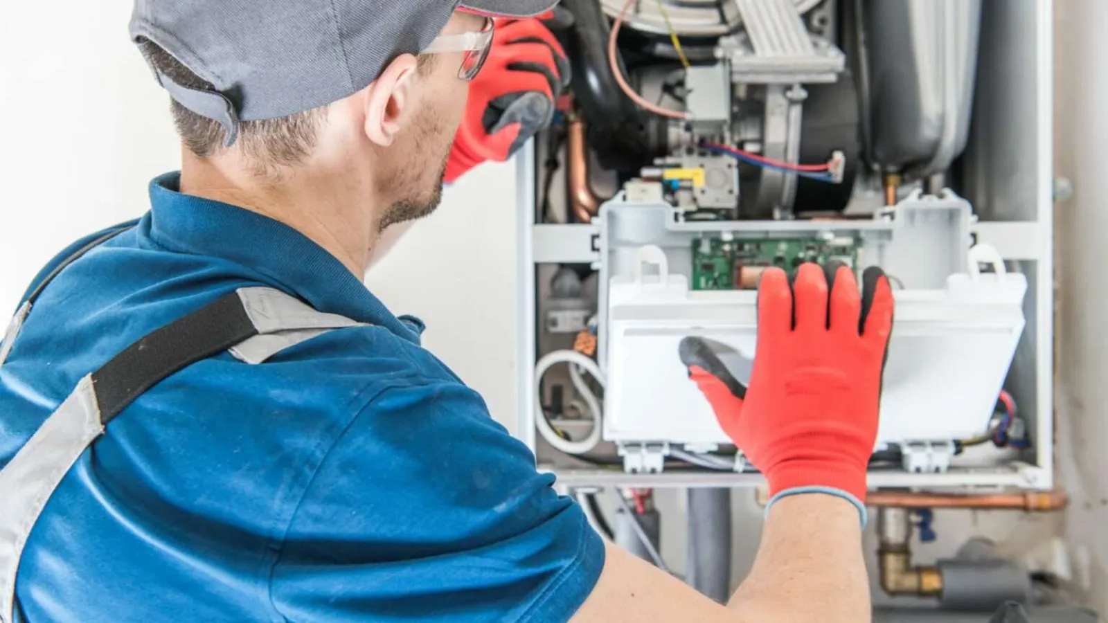 Technician wearing red gloves repairing or inspecting an open boiler heating system indoors.