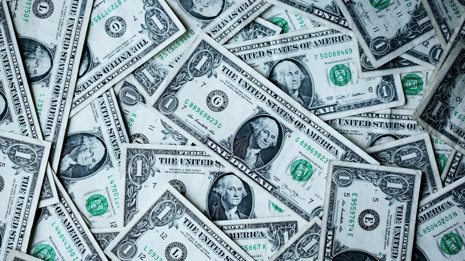 Pile of scattered one dollar US bills showing George Washington and green treasury seals.