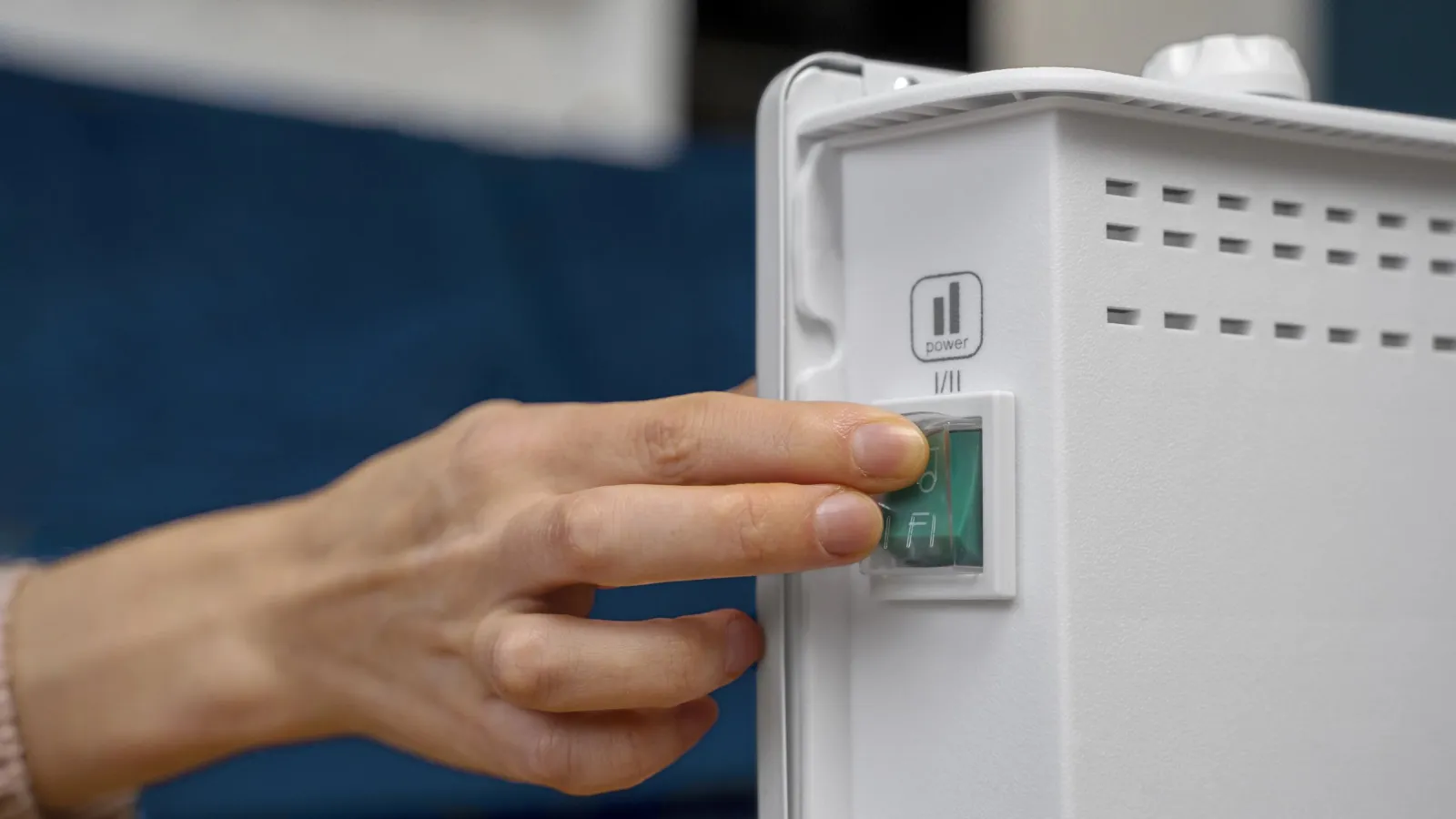 Hand pressing the power switch on a white electric heater in a cozy indoor setting.