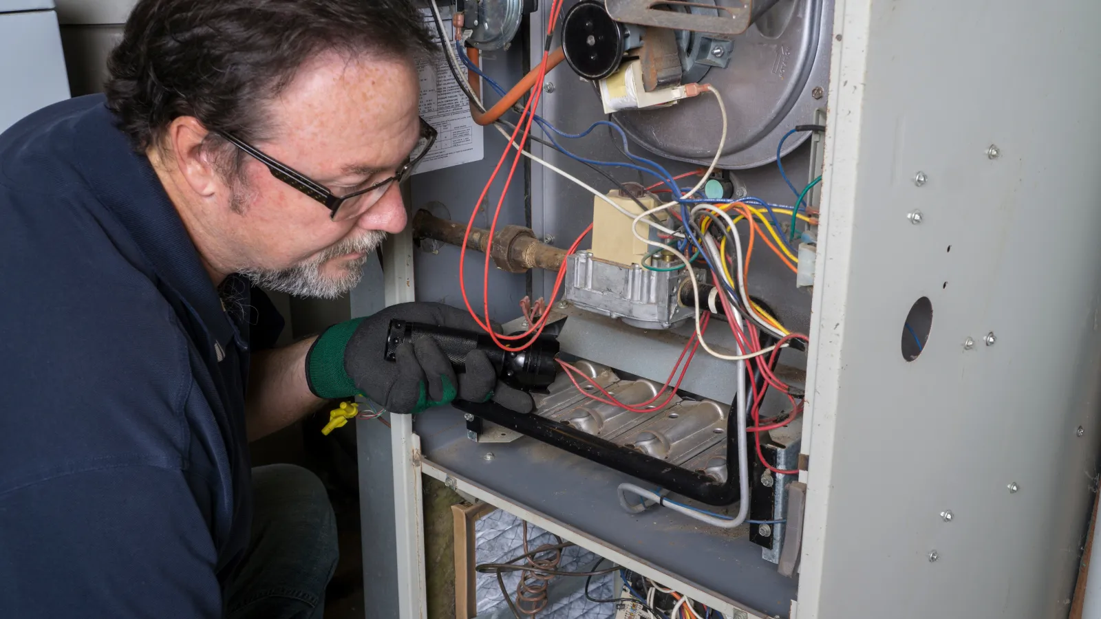 Technician inspecting and repairing a furnace with wires and components inside the metal casing.
