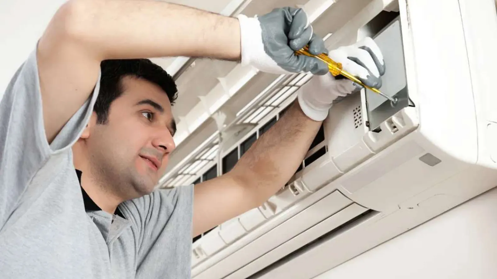 Technician with glasses inspecting and repairing an outdoor HVAC unit during daytime.