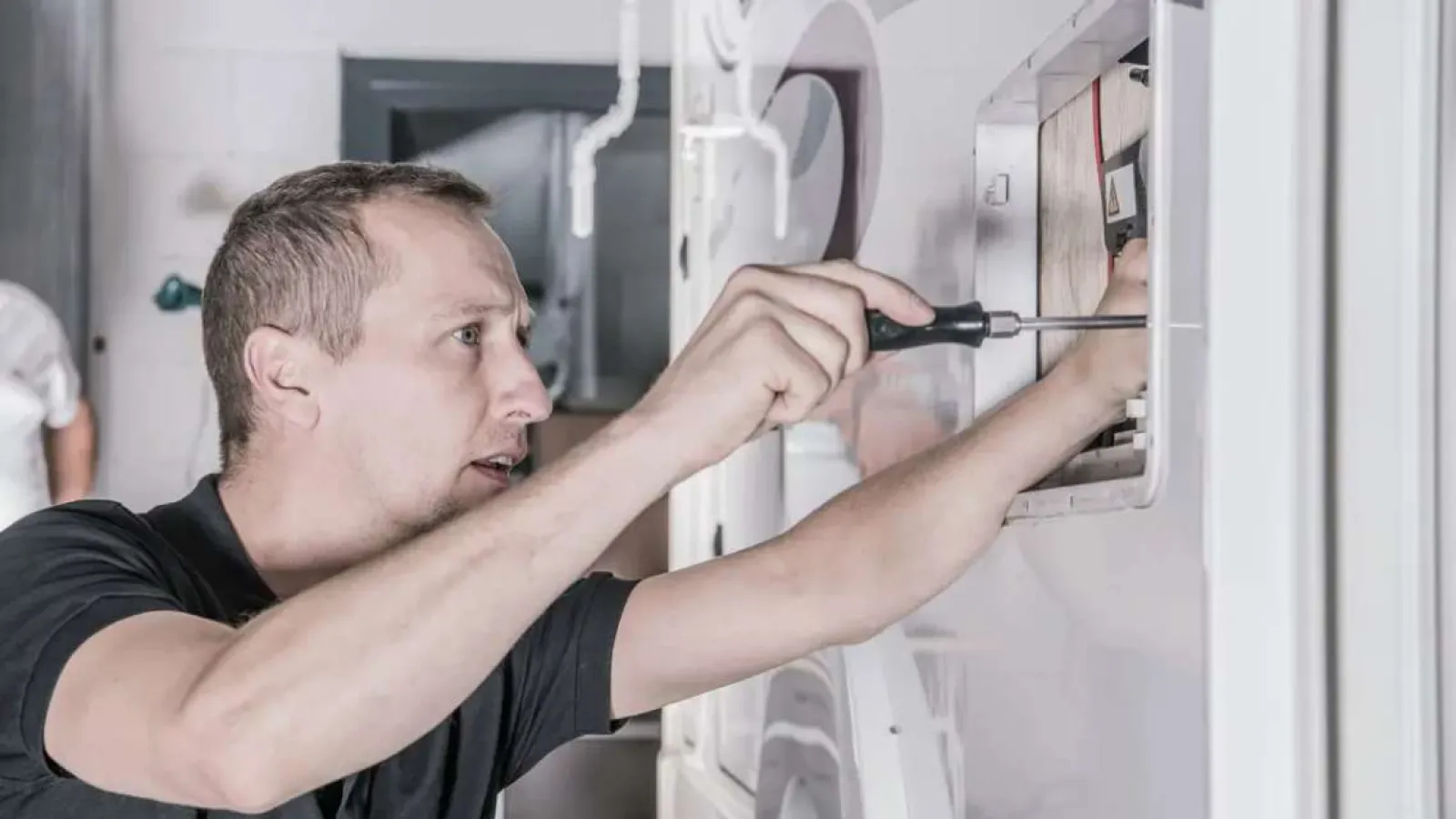 Technician with glasses inspecting and repairing an outdoor HVAC unit during daytime.