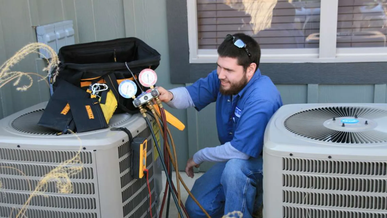 Technician with glasses inspecting and repairing an outdoor HVAC unit during daytime.